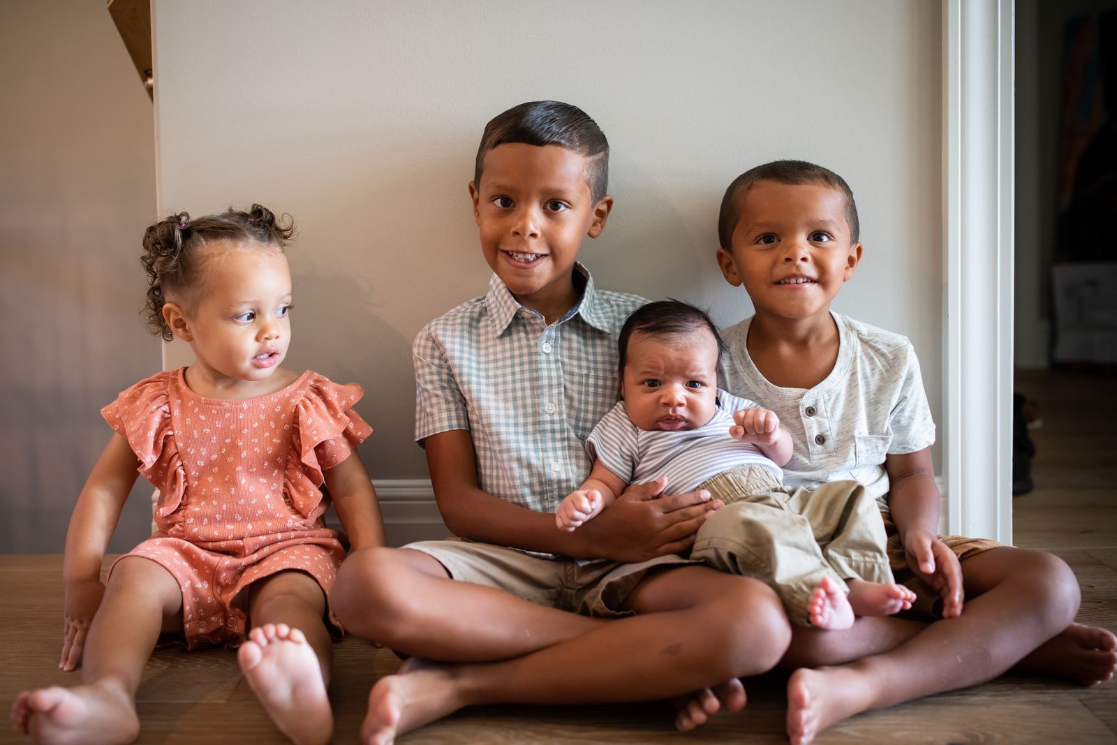 Four siblings, from a baby to an older child, sitting together on the floor